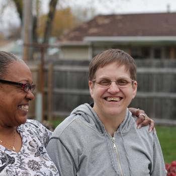 Two smiling women. One has her arm around the other.