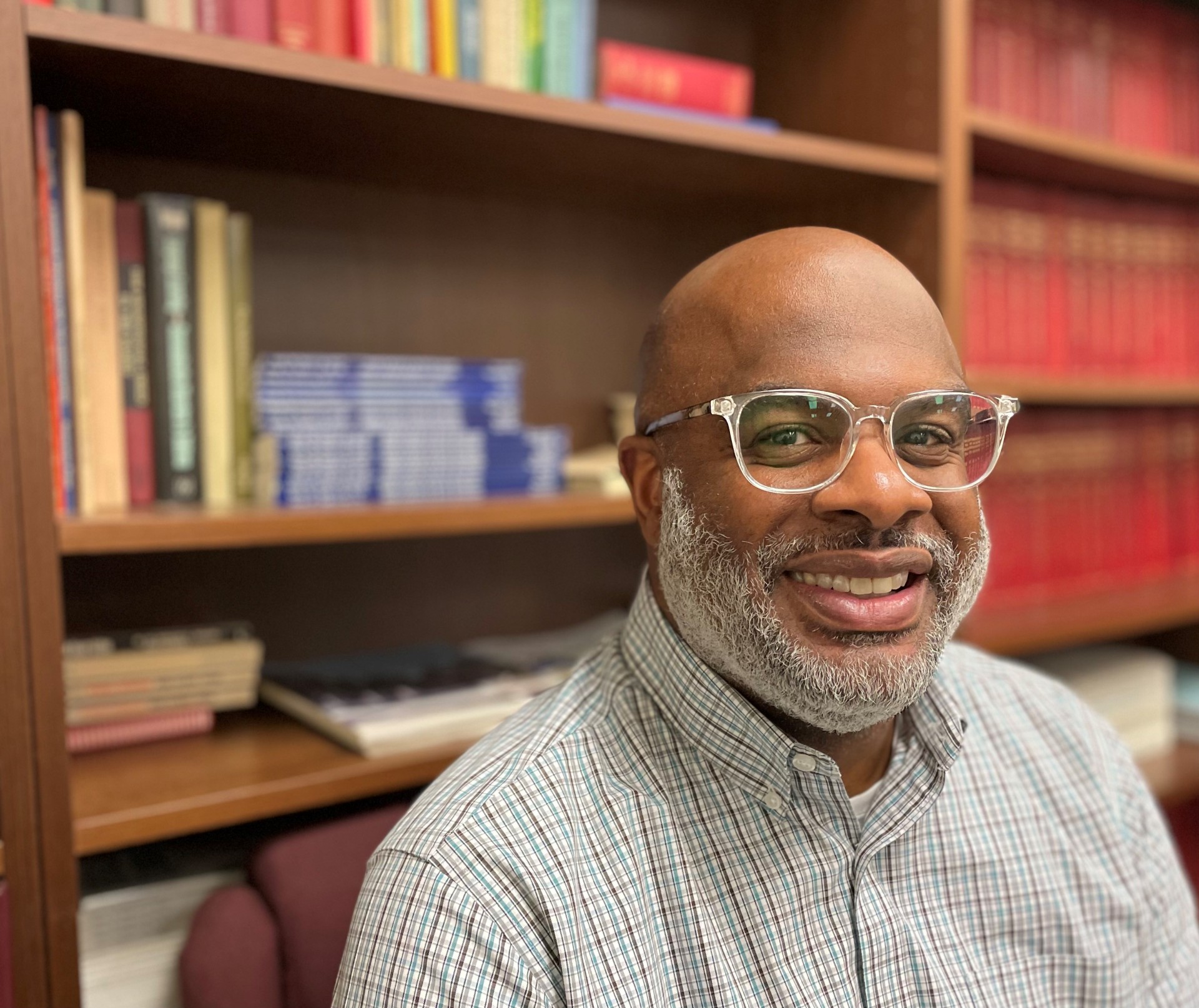 Smiling man with glasses and beard, sitting in front of book case