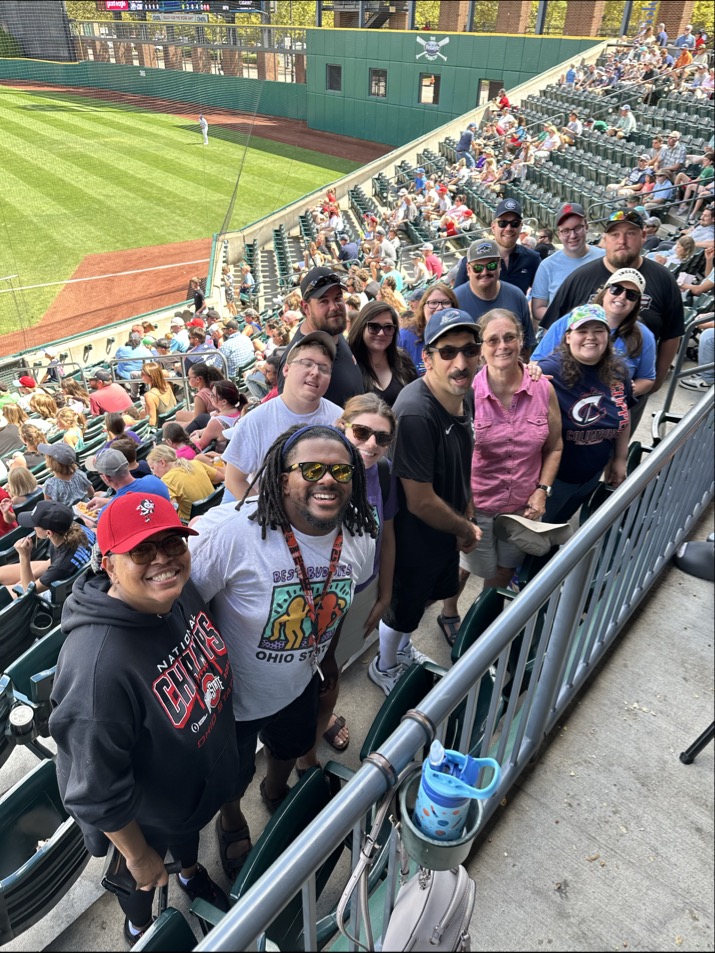 A group of friends standing and smiling in the seating area of a baseball stadium